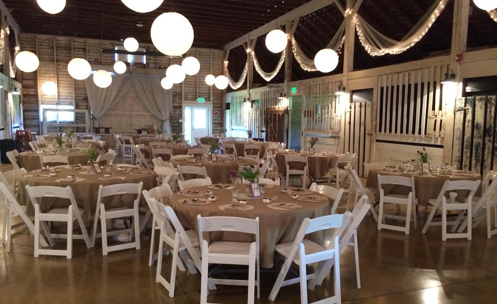 Barn set up for a wedding reception with round tables and paper lanterns