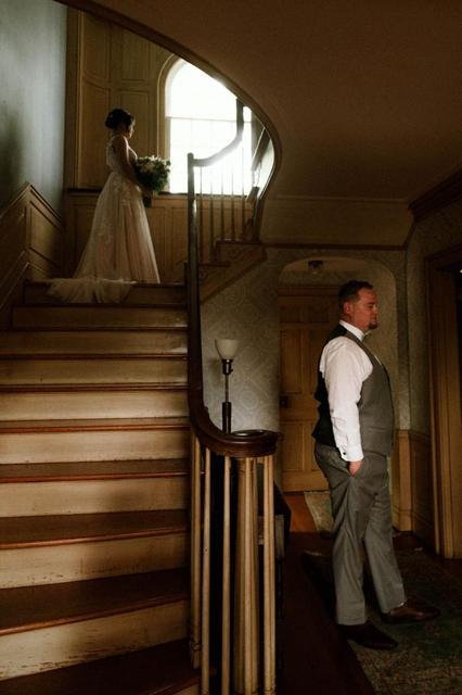 Bride at the top of the house staircase as the groom waits below