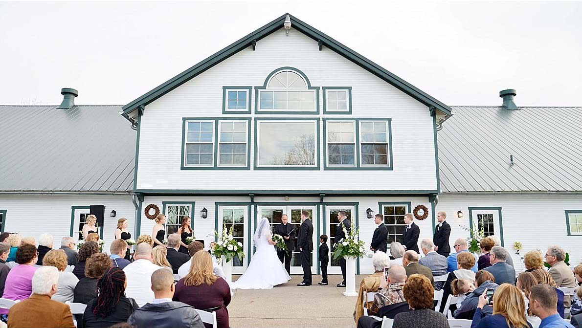 wedding ceremony in front of white barn