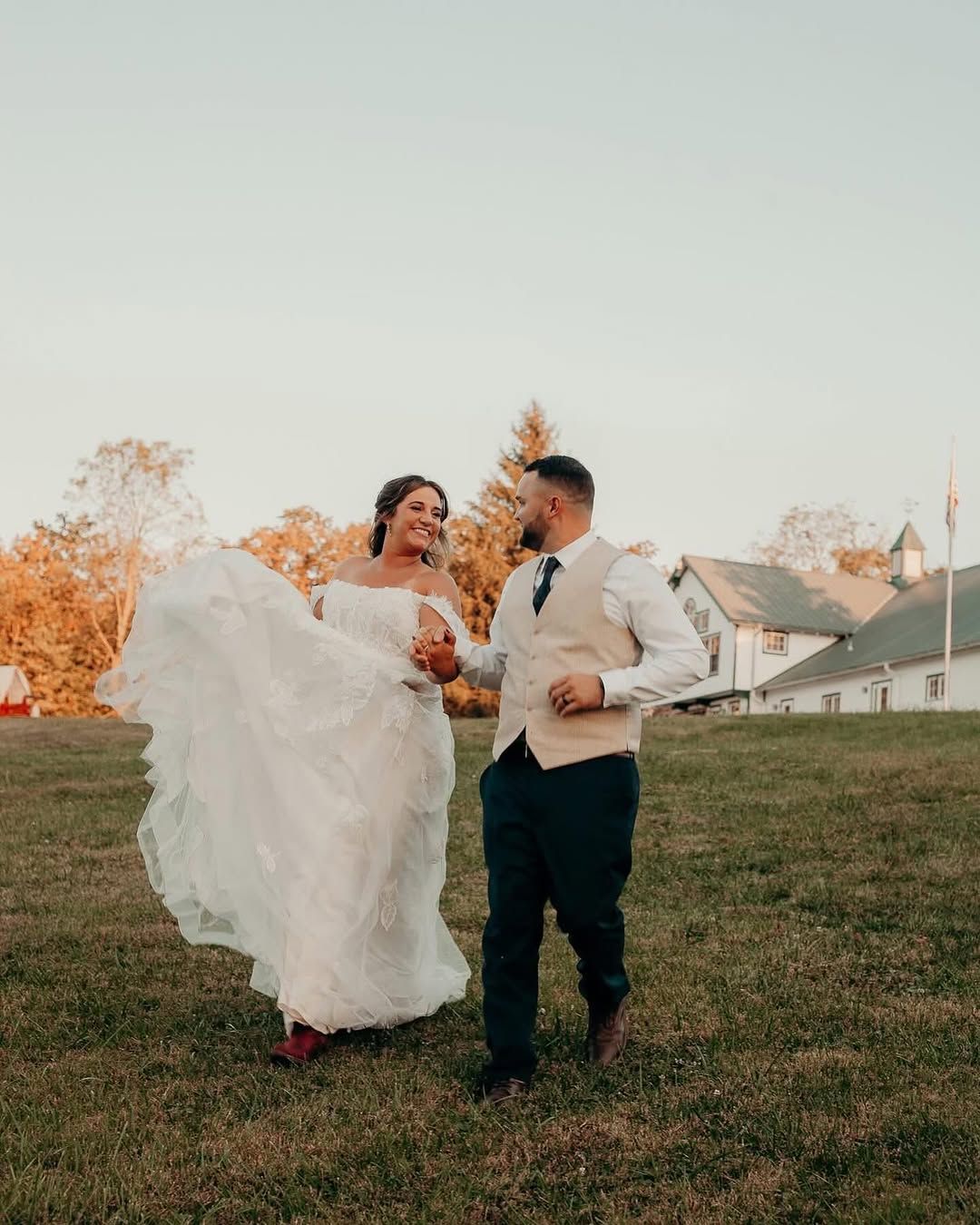 Bride and groom run across the lawn with the barn behind them