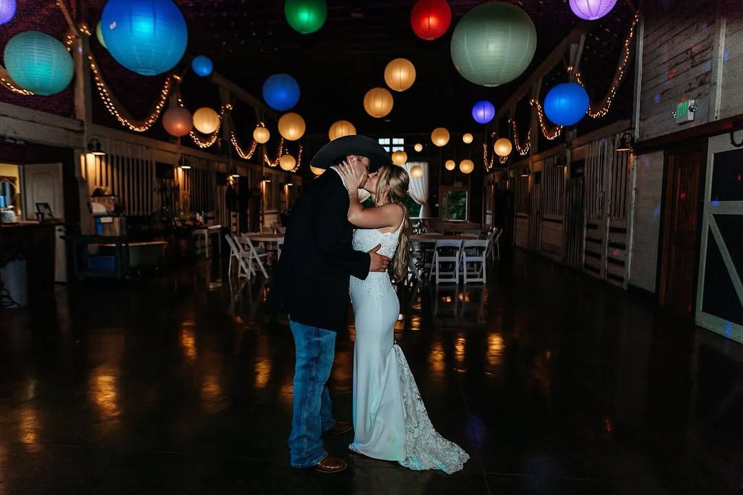 Couple in a cowboy hat kissing under colorful lanterns in the barn