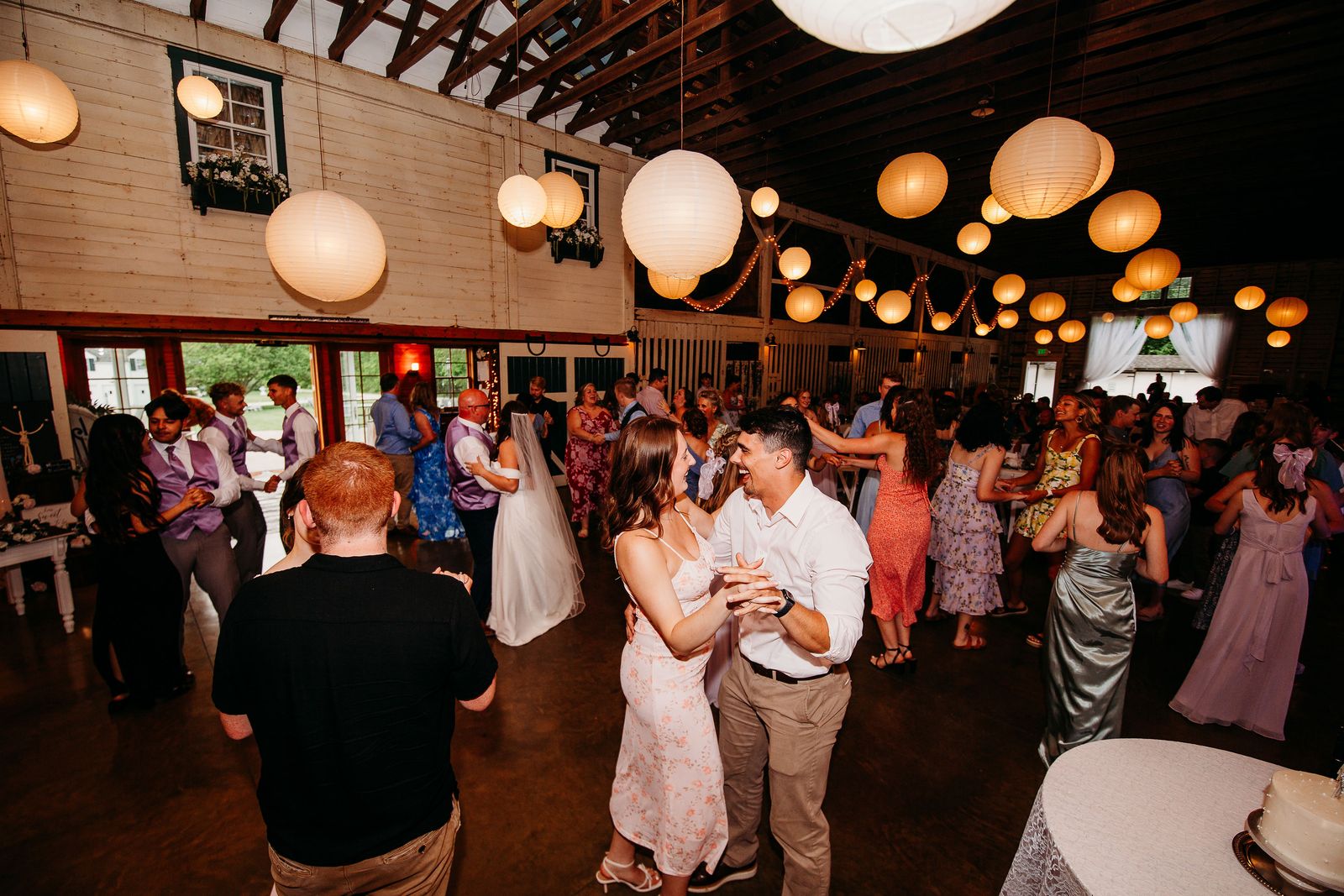 Guests fill the dance floor under paper lanterns in the barn