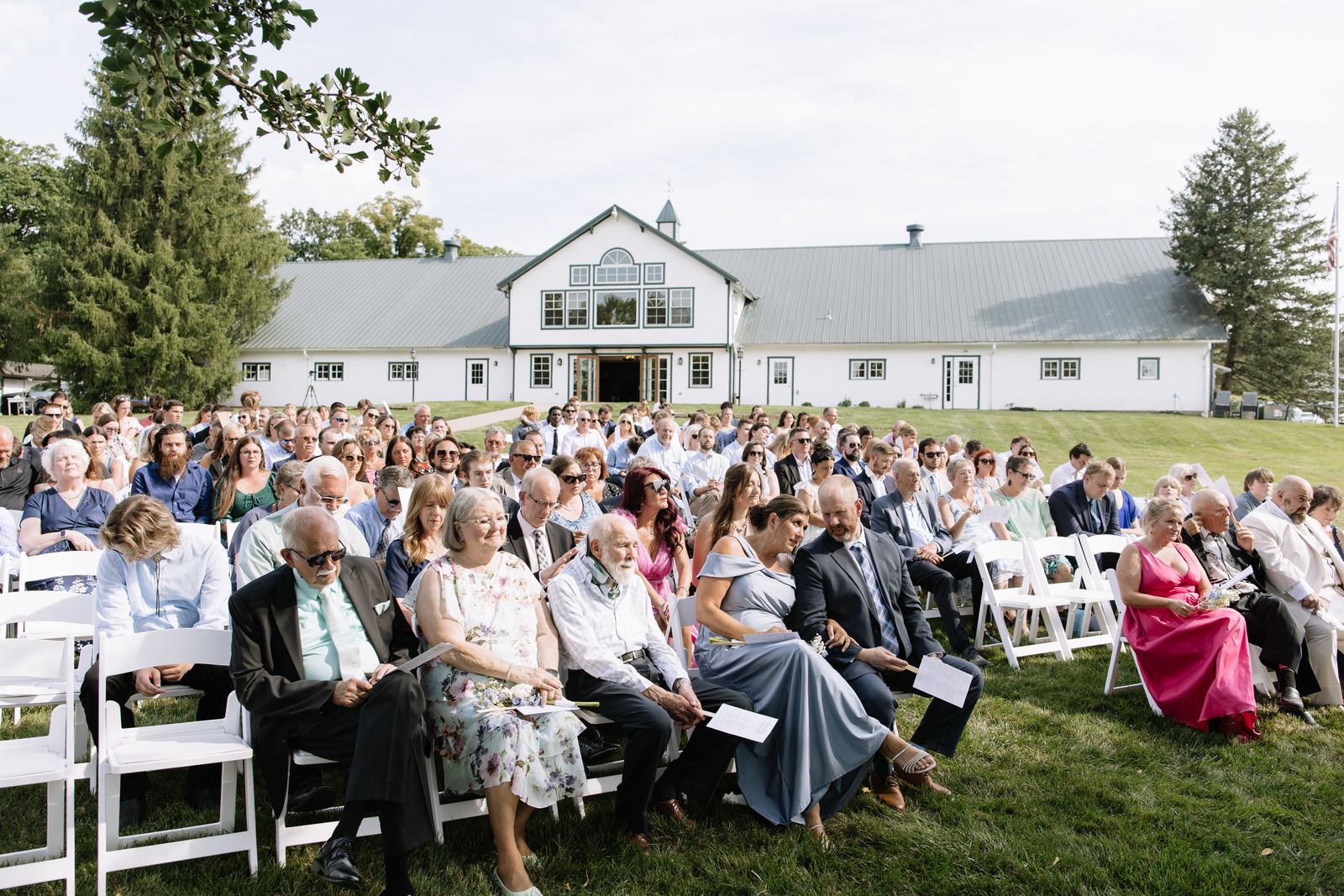 Guests seated for an outdoor ceremony on the lawn in front of the white barn