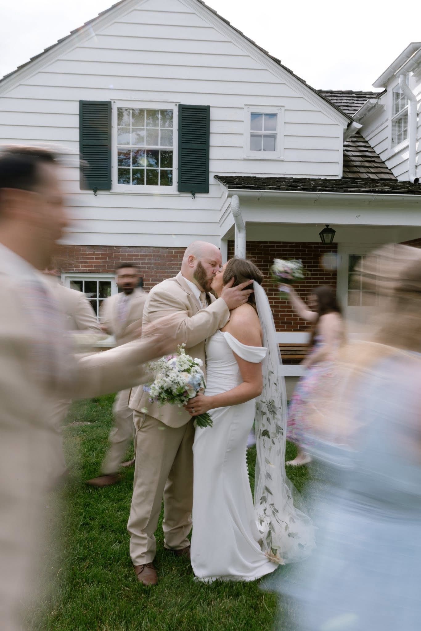 Couple kiss in front of the house as the wedding party celebrates