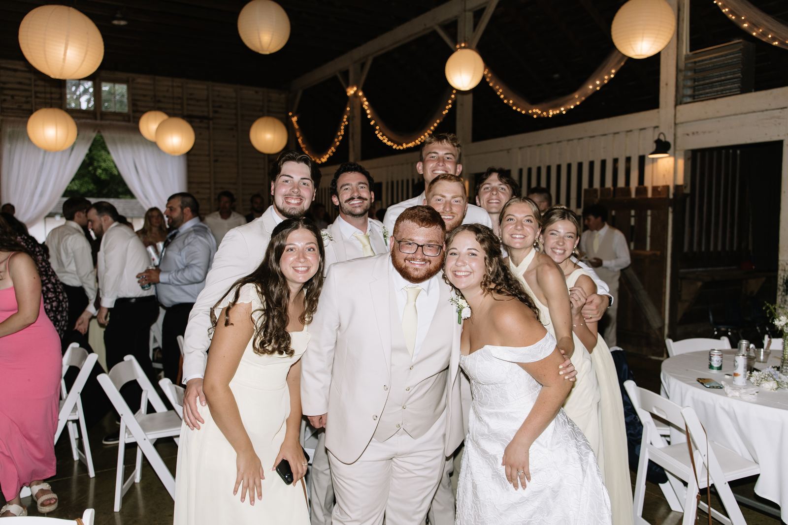 Wedding party smiling together in the barn reception under paper lanterns