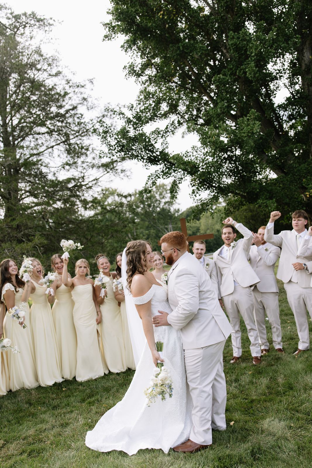 Bridesmaids and groomsmen cheering as the couple kisses on the lawn